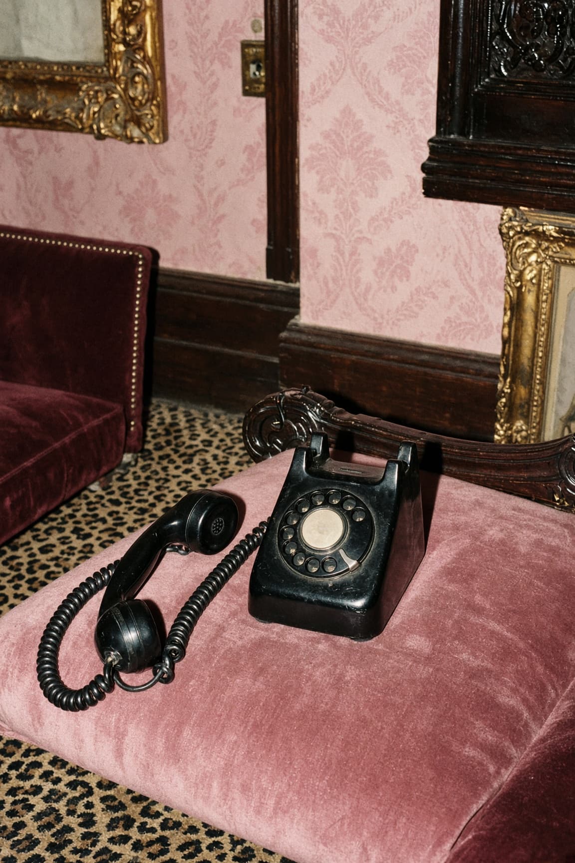 A vintage rotary telephone on pink velvet, receiver off the hook.